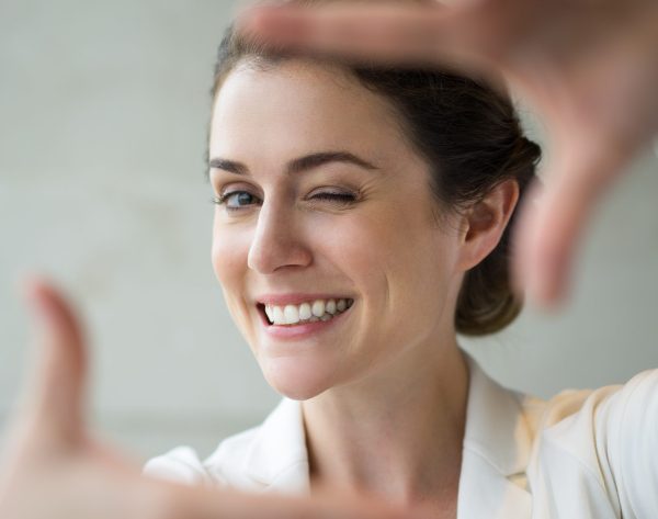 Closeup portrait of playful attractive middle-aged businesswoman looking at camera, smiling, making frame gesture and winking